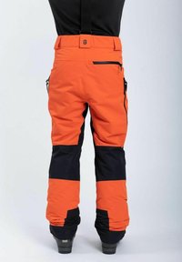 Oranssi ja mustat hiihtohousut, joissa on säädettävät hihnat, sivuviilto-taskut ja vahvistetut alaosat. Valmistettu kestävästä, säänkestävästä materiaalista.