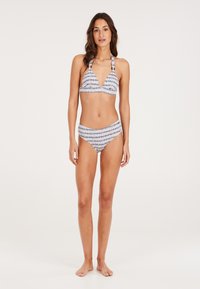 Bikini set s preklopnim vrhom, trokutastim gornjim dijelom i odgovarajućim visokim donjim dijelom gaćica. Ima bijelu podlogu s plavim i crnim geometrijskim uzorcima.