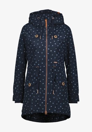 Veste de pluie navy avec des pois blancs, une capuche, une fermeture éclair à l'avant et deux grandes poches à rabat. Comprend des cordons de serrage et des éléments en métal couleur cuivre.