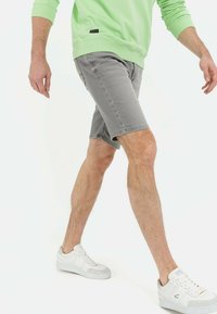 Graue Jeansshorts mit enganliegendem Schnitt, kombiniert mit einem hellgrünen Langarmhemd und weißen Sneakers mit grauen Akzenten.