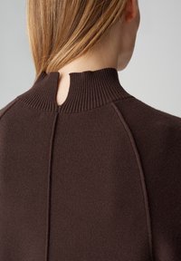 Bruine gebreide trui met een hoge geribbelde kraag, voorzien van een klein sleutelgatdetail aan de achterkant en een gestructureerde stof voor meer diepte.