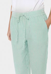 Pantalons légers rayés verts et blancs avec une taille élastique, un cordon de serrage ajustable et des poches latérales. Texture lisse.
