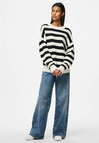 Maglione lavorato a maglia con righe orizzontali bianche e nere, maniche larghe e orlo a costine, abbinato a jeans di denim blu larghi e scarpe bianche.