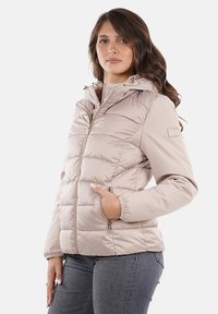 Giacca beige imbottita con cappuccio, dotata di zip frontale, polsini elasticizzati e tasche laterali; tessuto liscio con una leggera lucentezza.