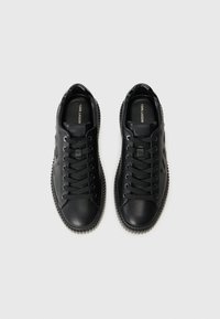 Baskets en cuir noir avec bout rond, fermeture à lacets et semelle en caoutchouc texturée. Présente un logo discret et une surface lisse.