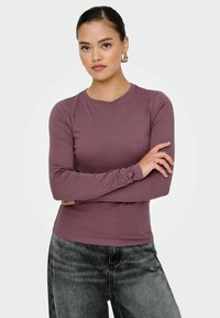 Top a maniche lunghe, aderente, di un mauve tenue, realizzato in tessuto morbido ed elasticizzato. Abbinato a jeans neri scoloriti. Semplice scollatura rotonda.