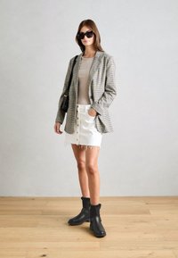 Rutigt kavaj i grått och svart, beige topp, vit denim-minikjol med knappfront och fransig fåll, svarta ankelstövlar med fuskpälskant.