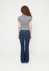 Γκρι κοντομάνικο μπλουζάκι με καρό σχέδιο και δετό κόμπο στο πίσω μέρος, συνδυασμένο με σκούρο μπλε τζιν καμπάνα με ραμμένες πίσω τσέπες.