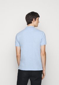Light blue polo shirt with a collar, short sleeves, and side slits, crafted from a smooth, textured fabric. No visible logos or patterns.