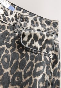 Jean en denim imprimé léopard avec un motif beige clair et gris foncé, doté d'une poche avant et d'une fermeture à boutons argentés.