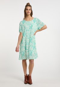 Vestido verde menta con un patrón de paisley, mangas cortas y un corte relajado, combinado con botas marrones hasta el tobillo. Textura de tela suave.