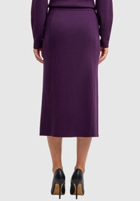 Paarse geribbelde gebreide midi-rok met een aangesloten taille en rechte silhouet, gecombineerd met zwarte hoge hakken. De textuur is glad en gestructureerd.