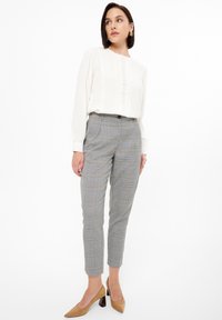 Blusa blanca con tejido texturizado y pequeños detalles, combinada con pantalones de cuadros grises de corte slim y largo hasta el tobillo, acentuada por tacones marrones.