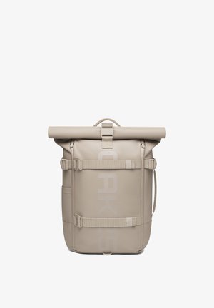 Sac à dos beige à rabat enroulable avec bretelles ajustables, poignée latérale et discret logo vertical sur le panneau avant.