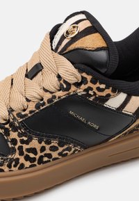Baskets Michael Kors avec lacets beiges, panneaux en cuir noir, accents imprimé léopard et zèbre, et semelle en caoutchouc marron.