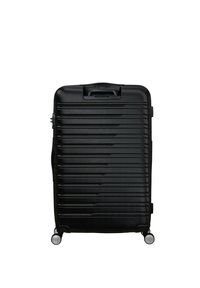 Valigia rigida nera con scanalature verticali, maniglia superiore e quattro ruote per la mobilità. Texture liscia e design aerodinamico.