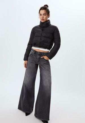 Svart kort pufferjacka med hög krage, kombinerad med vida grå jeans. Strukturerad tyg med synliga sömmar och fickor.