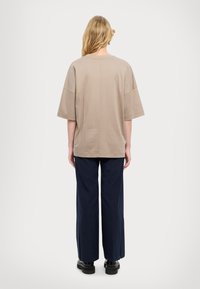 T-shirt oversize beige con maniche corte, caratterizzato da un collo rotondo e un orlo dritto, abbinato a pantaloni palazzo blu navy e scarpe nere.
