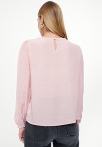 Blusa rosa chiaro a maniche lunghe realizzata in tessuto texturizzato, con apertura a forma di chiave sul retro e polsini con bottoni.