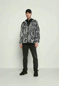 Leichte schwarz-weiße Jacke mit Muster, Kapuze, Reißverschluss, elastischen Bündchen, kombiniert mit schwarzen Hosen und Sneakers.