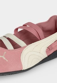 Κοντινή λήψη ροζ και λευκού μπαλαρίνας Puma με ελαστικά λουράκια και μαύρη σόλα σε λευκό φόντο.