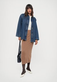 Mørkeblå denimjakke med lange ermer, kneppet. Beige strikket midi-skjørt, tettsittende. Svart håndveske, gjennomsiktige strømpebukser, og hvite spissede sko.
