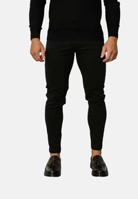 Pantalons noirs slim-fit en tissu lisse, avec un design fuselé et une taille élastique. Associés à des mocassins noirs.