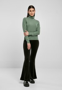 Bluză mint cu gât înalt, cu mâneci lungi, asortată cu pantaloni negri cu evazare și cizme masive negre; textură de țesătură netedă pe tot parcursul.