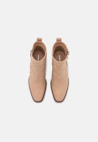 Beige suede ankle boots with a pointed toe and a side zipper, featuring a textured finish and a low stacked heel.