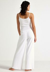Hvid, ribbet tanktop og matchende vide bukser, der har et kort design og rå kanter for et struktureret look.