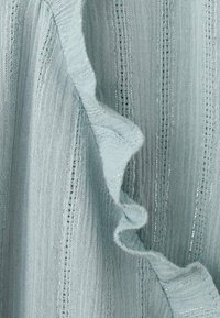 Light blue fabric with a textured, ribbed pattern, featuring ruffled edges and subtle metallic thread accents. Soft and airy appearance.