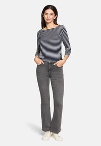 Navy- und weiß gestreiftes Bootsausschnitt-Oberteil mit langen Ärmeln, kombiniert mit grauen Schlagjeans und weißen Sneakers. Einfaches Design, lässige Passform.