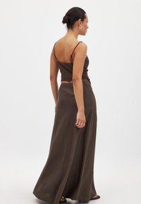 Brun tvådelad outfit bestående av en figurnära kort topp med tunna band och en golvlång kjol, båda i ett lätt, strukturerat material.