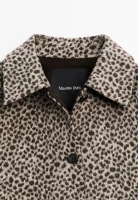 Collare di un cappotto di lana con stampa leopardata, con due bottoni neri e un'etichetta nera di Massimo Dutti su sfondo bianco.
