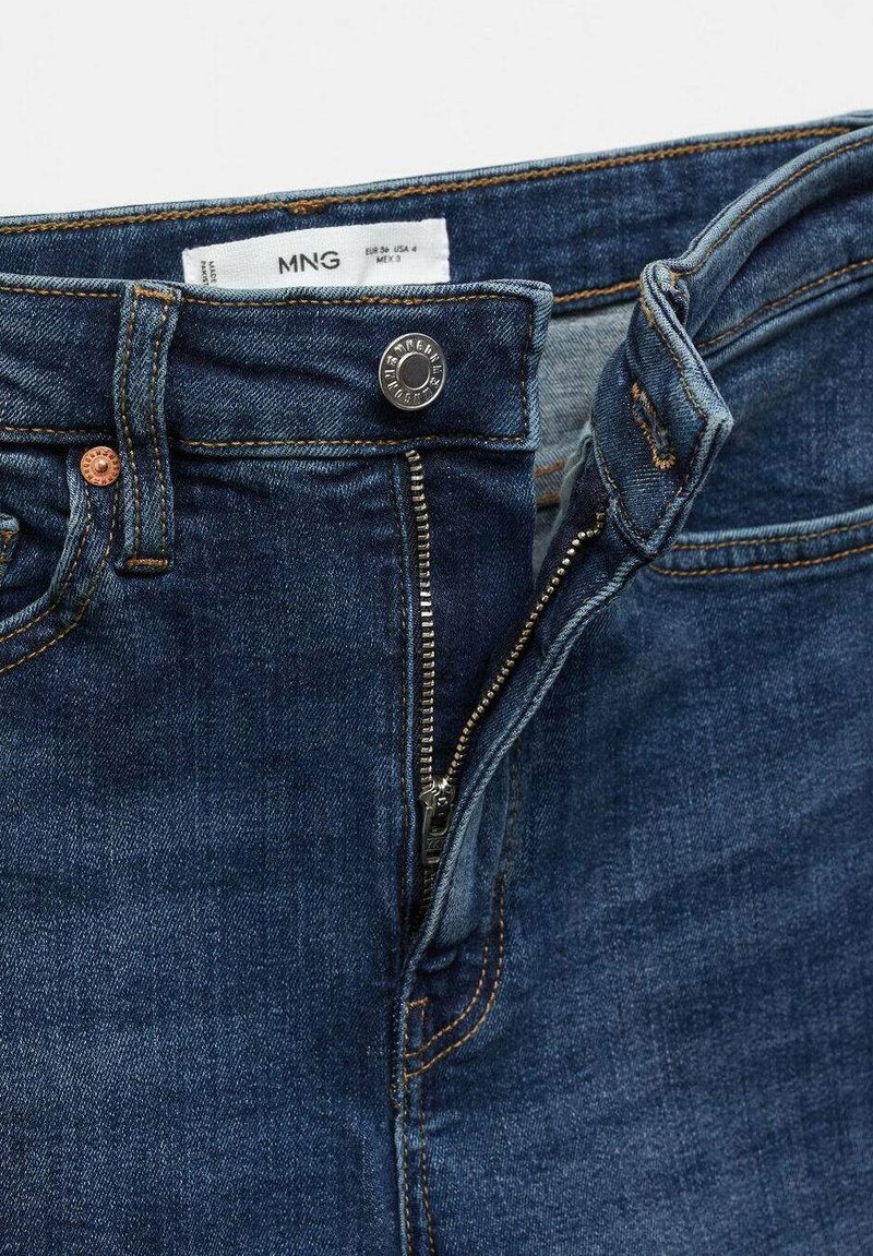 Dunkelblaue Denim-Jeans mit Reißverschluss, Metallknopfverschluss und kontrastierenden gelben Nähten. Markenlabel innen im Bund sichtbar.