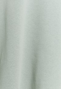 Vaaleanvihreä t-paita, jossa on pehmeä ja teksturoidun tuntuinen kangas. Suunnittelu on yksinkertainen ilman kuvioita, korostaen sileää pintaa ja hillittyä väriä.