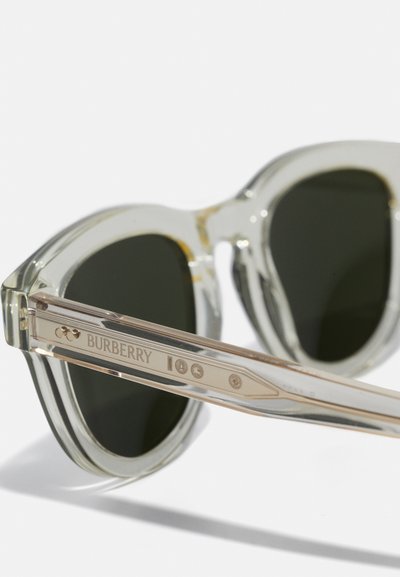 Óculos de sol transparentes cinza claro com lentes escuras, apresentando um design retangular largo. O logotipo da Burberry está gravado na hastes.