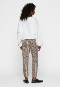 Witte oversized sweatshirt, bruine slangenprintbroek en zwarte loafers. Soepele stof, losse pasvorm en gedetailleerd patroon op de broek.