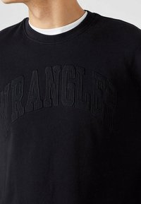 Felpa nera con logo "WRANGLER" in rilievo ricamato tono su tono. Design classico con collo rotondo e tessuto morbido.