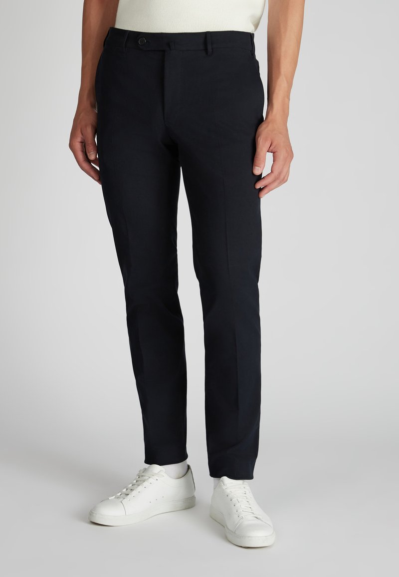 Chinos blu scuro realizzati in tessuto leggero, con una vestibilità slim, tasche laterali e chiusura con zip. Abbinati a sneakers bianche.