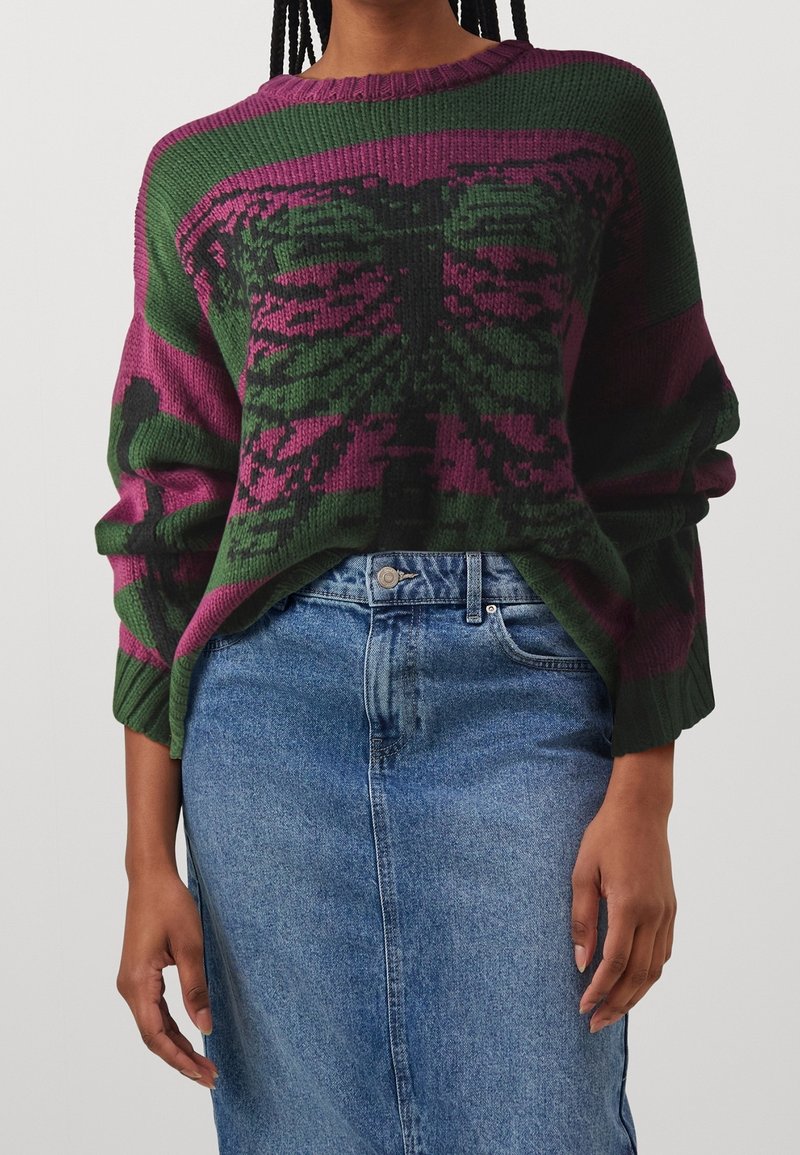 Übergrößter grüner und lila gestrickter Pullover mit Floral-Muster. Rippkragen und -bündchen, kombiniert mit einem hellblauen Jeansrock.
