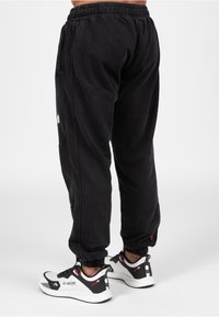Zwarte joggingsbroek met een elastische tailleband en manchetten. Inclusief zijzakken en een logodetail aan de linkerkant. Draag met sportieve zwart-witte schoenen.
