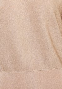 Pull en maille beige avec un design côtelé texturé. Le tissu a une légère brillance, avec une finition lisse et une coupe décontractée.