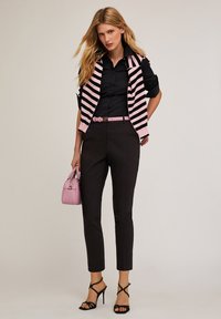 Camisetta nera sotto un gilet a righe rosa e nere, pantaloni neri, cintura rosa e una piccola borsa rosa. Presenta tacchi alti neri con cinturini.