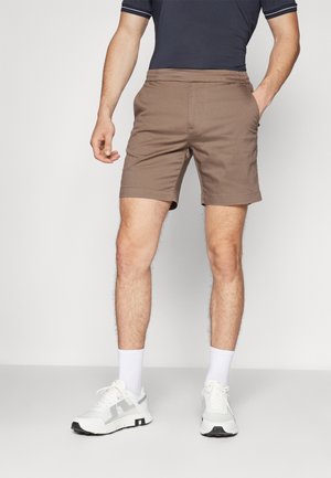 Brown shorts with an elastic waistband, side pockets, and a simple design. Worn with white sneakers and ankle-length socks.