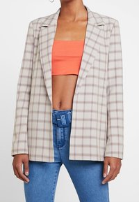 Veste à carreaux beige avec une coupe ajustée, dotée d'un revers cranté, d'une fermeture boutonnée simple et de deux poches avant.