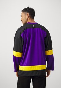 Violeta un melna garā piedurkne basketbola krekls ar dzelteniem akcentiem. Aizmugurē ir NBA logotips un tas ir ar brīvu piegriezumu.