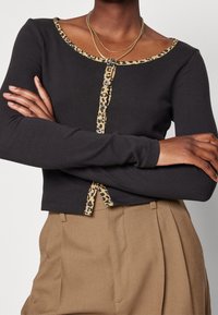 Svart långärmad topp med leopardmönstrad halsringning och knappslå, ihop med beiga byxor. Mjuk tyg och figursydd design.