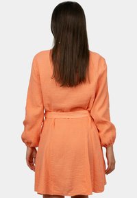 Abito color pesco con tessuto testurizzato, maniche lunghe, vita con cintura e gonna a campana, visto da dietro.