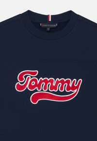 Marinblå sweatshirt med tredimensionell röd och vit "Tommy"-logotyp. Har en ribbad rund halsringning och subtil sömnad över bröstet.